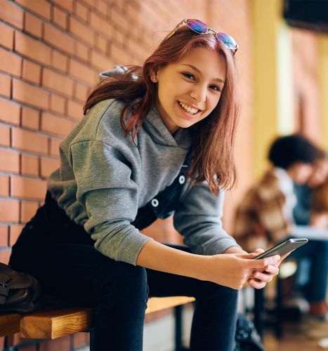 Smiling teenager sitting on a bench holding phone