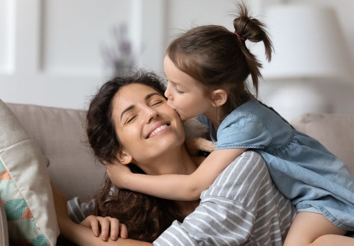 Daughter kissing mother's cheek on couch