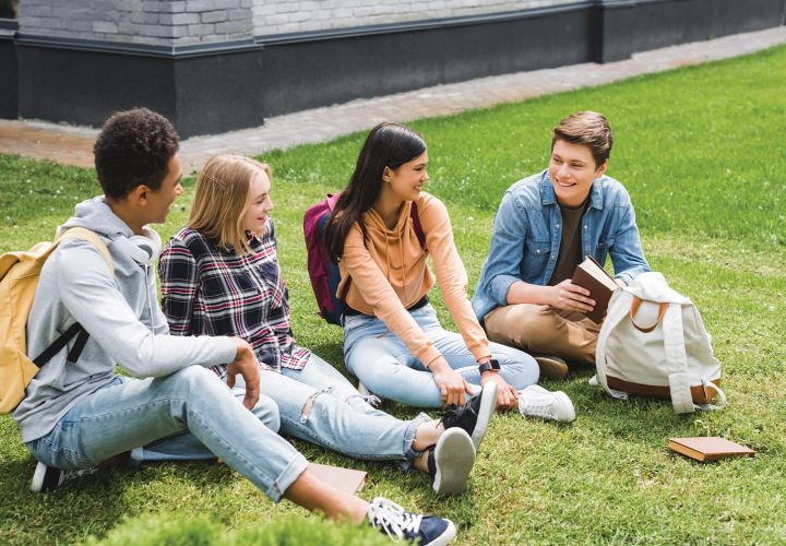 Teenagers sitting on grass with school supplies
